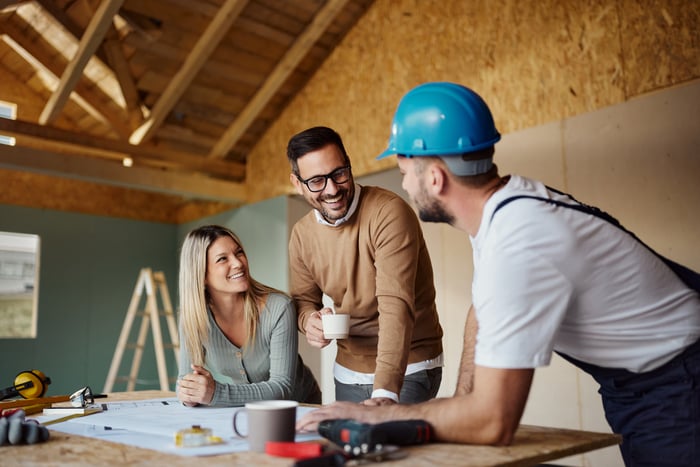 Smiling people chat with a person building their house.