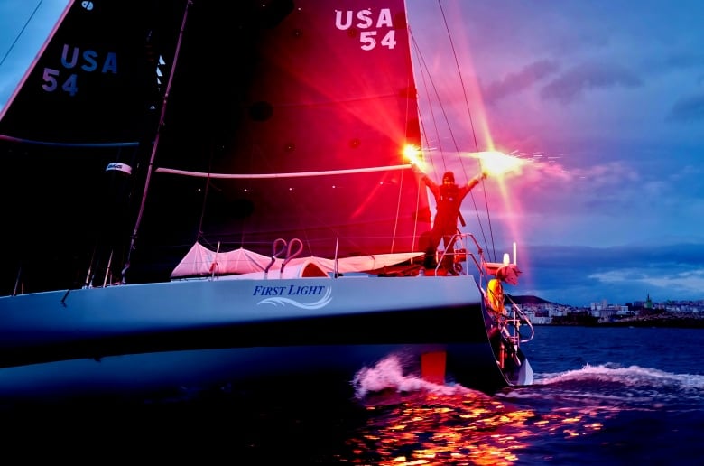 A woman stands on a sailboat with flares in each hand.