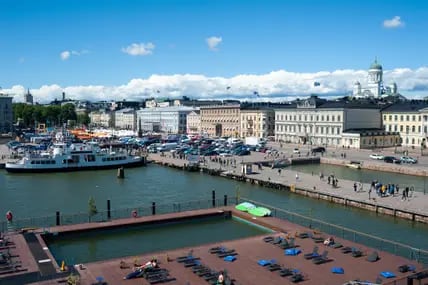 Blick über das Sonnendeck und einen Außenpool von Allas Seapool in Hesinki, im Hintergrund das Stadtpanorama mit Dom