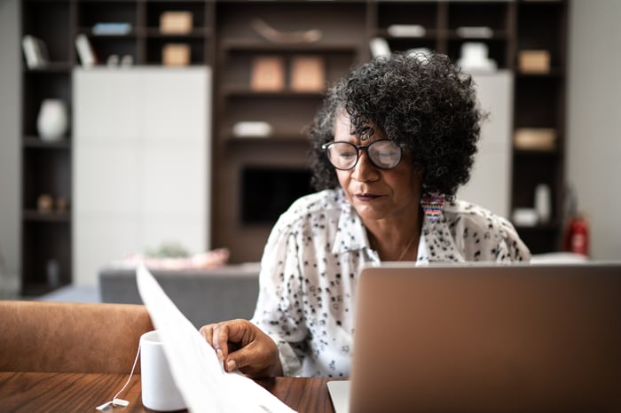 Adult looking at laptop and financial documents.