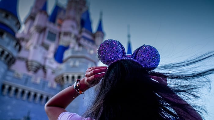 Someone wearing purple mouse ears outside Disney castle.