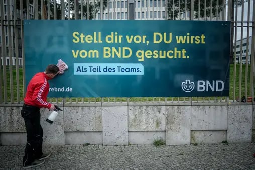 14.03.2024, Berlin: Ein Arbeiter säubert ein Plakat der neuen Imagekampagne des Bundesnachrichtendienstes (BND) mit der Aufschrift «Stell dir vor, du wirst vom BND gesucht» am Zaun der Zentrale des Dienstes. 

Normalerweise sucht der Bundesnachrichten-Dienst (BND) Kriminelle. Doch gerade sucht er auch neue Mitarbeiterinnen und Mitarbeiter. Darum geht auf diesem Plakat. (zu dpa: «Als Spion oder Spionin arbeiten») Foto: Kay Nietfeld/dpa - Honorarfrei nur für Bezieher des Dienstes dpa-Nachrichten für Kinder +++ dpa-Nachrichten für Kinder +++