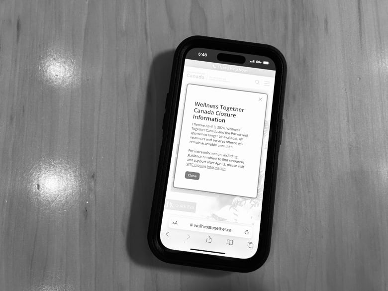 Black and white photo of phone showing an alert saying "Wellness Together Canada Closure Information"