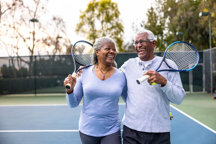 Laughing couple holding tennis rackets.