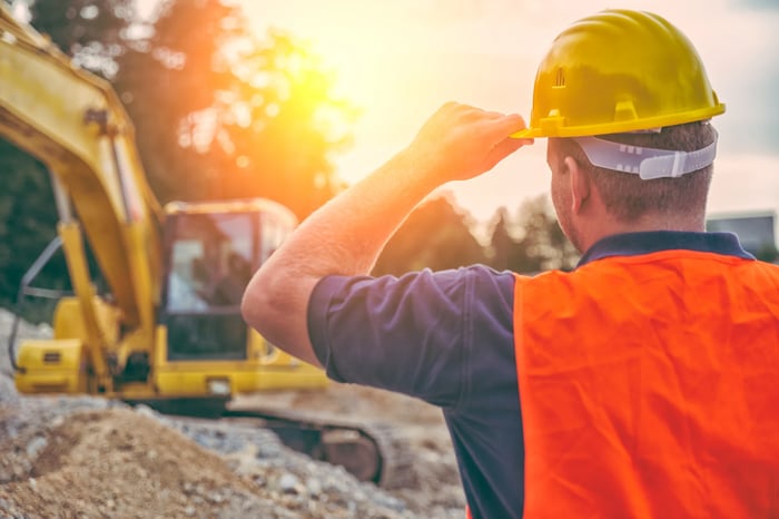 A person with a hard hat on stands in front of heavy machinery.