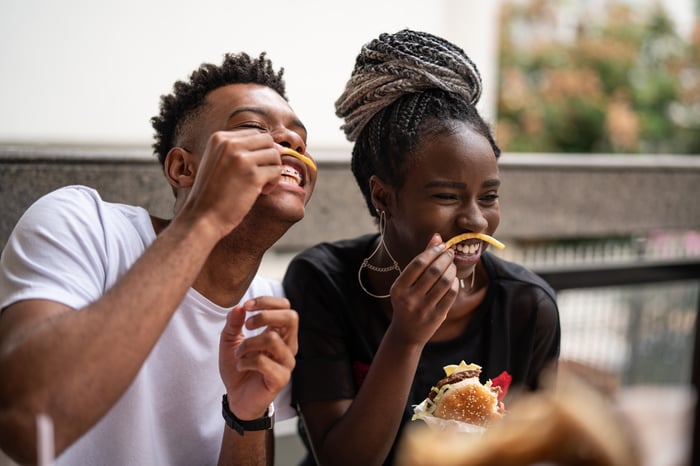 Two people sharing a burger and fries.