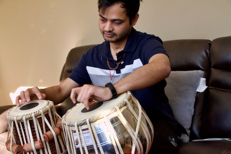 A young man plays a larger and smaller drum with each hand.