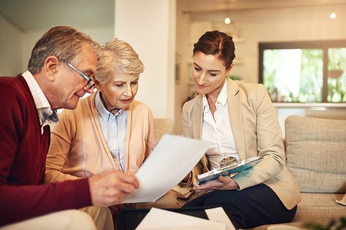 A mature couple discusses paperwork with a businesswoman in a home.