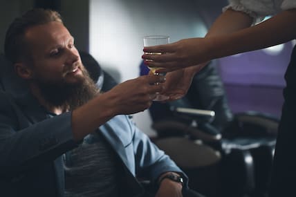 Flugbegleitung serviert Wein an Geschäftsmann im Flugzeug.