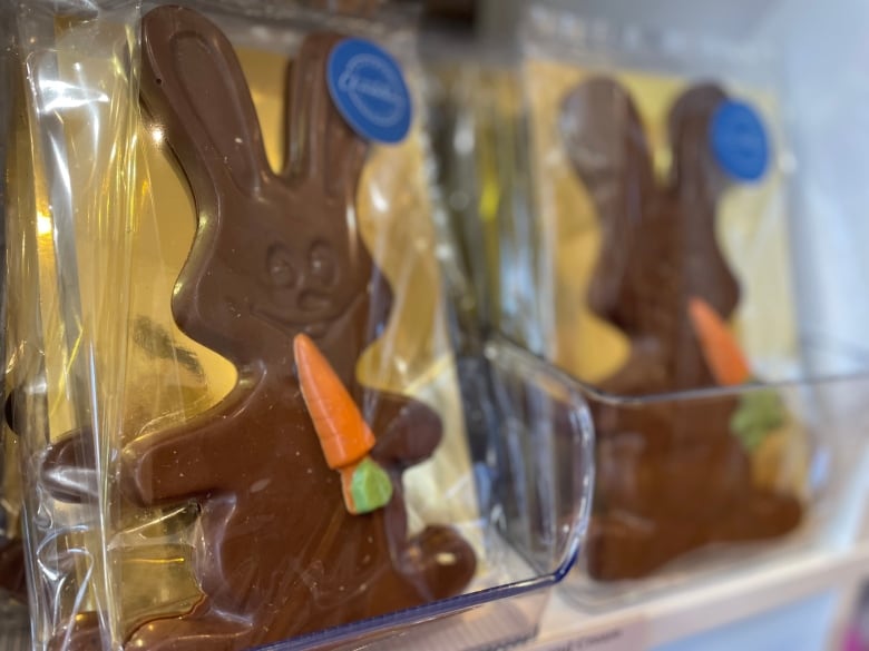 Chocolate treats in the shape of a bunny biting into a carrot are displayed in cellophane wrapping on a store shelf.