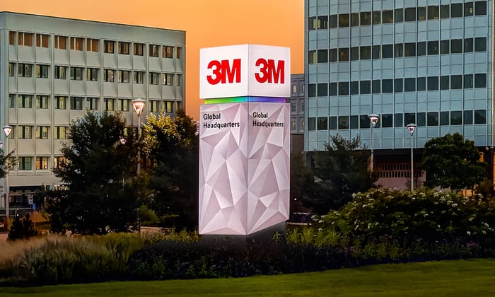 A monument sign with the 3M logo on it at night with the company headquarters in the background.