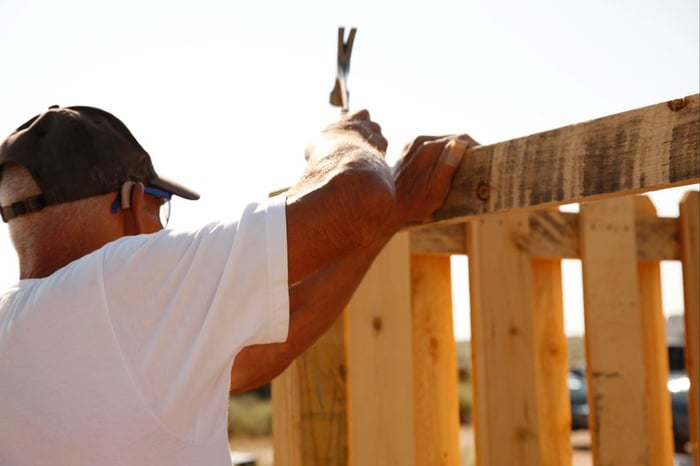 A person hammering nails into a new wooden fence.