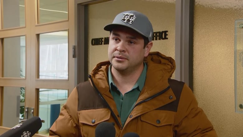 A man in a grey baseball cap speaks to reporters.