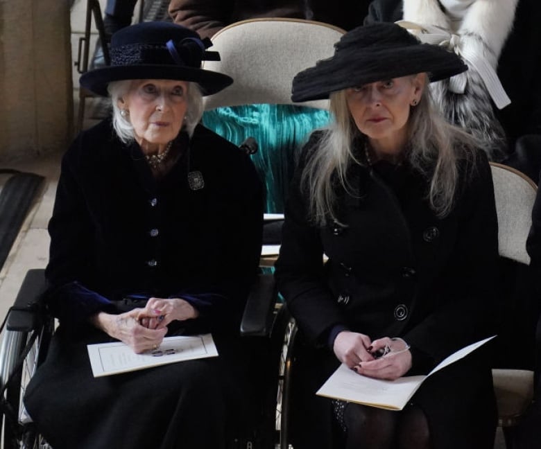 Three people holding programs sit on chairs in a large church.