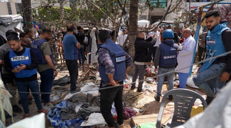 Palestinians and local members of the media check the damage at a makeshift camp for displaced people.