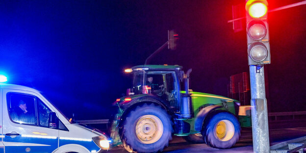 Nachts: Polizei mit Blaulicht im Vordergrund und eine Ampel steht auf Rot, dahinter ein Traktor