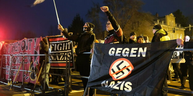 Linke Aktivisten in Chemnitz heben eine Fahne und die Faust hinter einem Transparent mit einem durchgestrichenen Hakenkreuz und der Aufschrift 