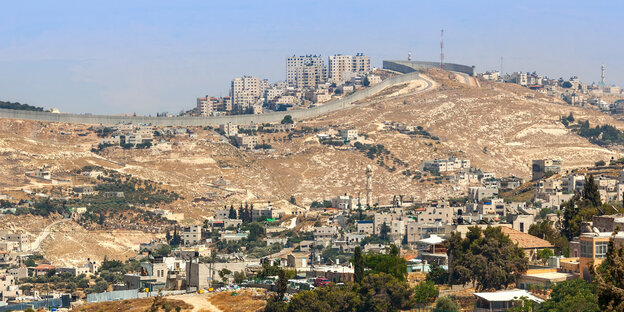 Blick auf die Landschaft bei Jerusalem, im Vordergrund ein palästinensischer Ort, Sonne scheint auf sandige Landschaft, blauer Himmel