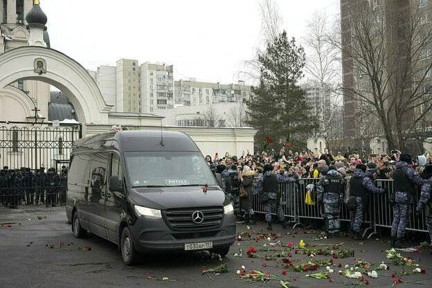 Ein Lieferwagen mit dem Sarg des russischen Oppositionsführers Alexej Nawalny verlässt die Kirche, hinter einem Absperrgitter stehen Trauernde, bewacht von Polizisten, auf der Straße liegen Blumen