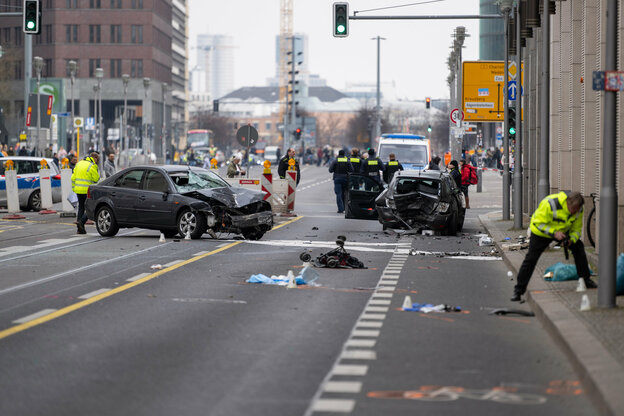 Eine große Straße ist rund um zwei kaputte Autos abgesperrt. Polizist:innen stehen hinter der Absperrung. Ein zerstörter Buggy liegt auf dem Asphalt.