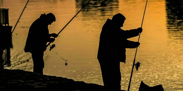 Silhouetten von zwei Anglern bei Sonnenuntergang