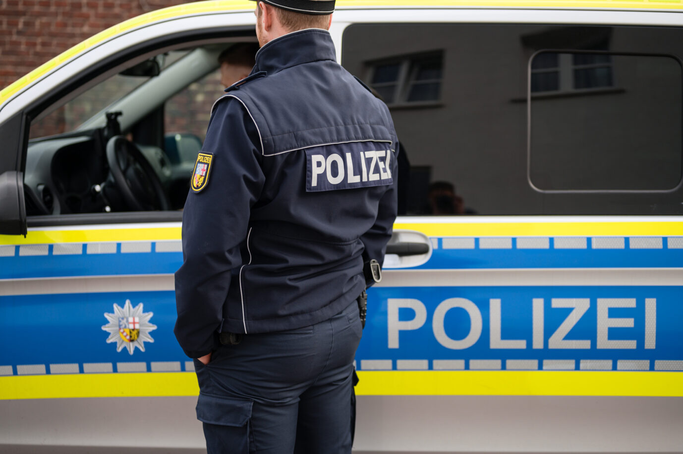 Ein Polizist steht vor einem Einsatzfahrzeug im Saarland. Bulgaren stürmen Schule.