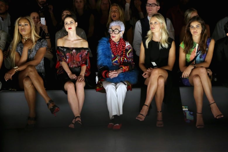 People are seen seated in the front row of a fashion show.