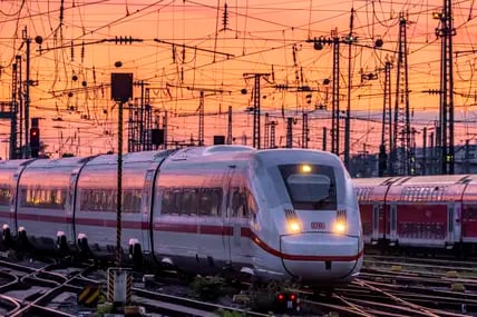 Ein ICE und ein Regionalzug fahren bei Abenddämmerung in den Bahnhof ein.