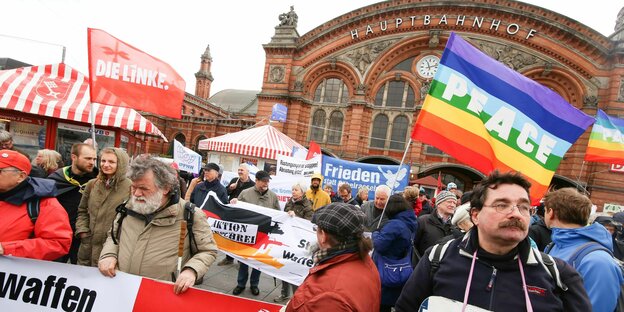 Teilnehmende beim Ostermarsch 2017 mit Plakaten und Fahnen vor dem Bremer Hauptbahnhof. Zu sehen sind unter anderem eine 