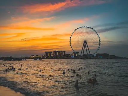 Blick auf die Skyline von Dubai mit dem Ain Dubai Riesenrad vor einem Himmel mit Abendstimmung