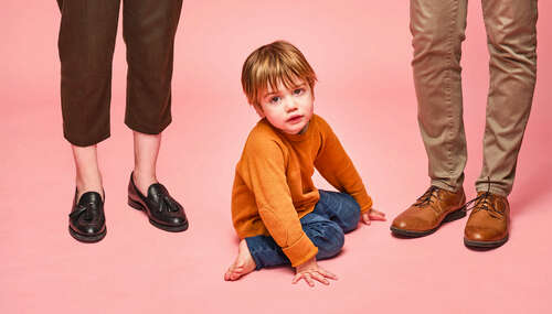 A photo of a child sitting on the ground between two parents' legs.