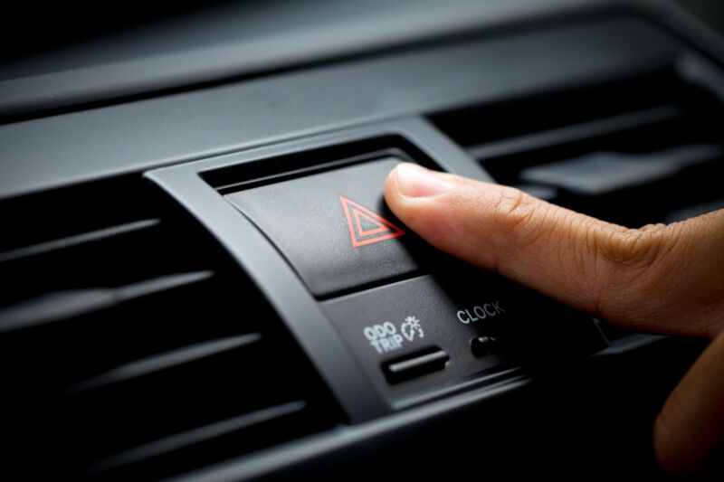 man pushing red triangle warning car button