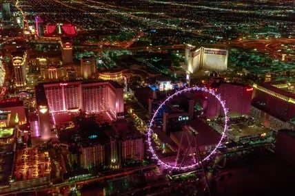 Blick von oben auf das nächtlich erleuchtete Las Vegas mit dem Riesenrad High Roller im Vordergrund