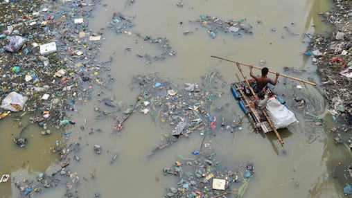 27.07.2023, Bangladesch, Sylhet: Ein Vater rudert mit seinem Sohn auf einem handgefertigten Floß und sucht im mit Plastikmüll gefüllten Kanal von Kazir Bazar in Sylhet nach Recyclingprodukten aus Plastik. Dieser Kanal ist direkt mit dem Surma-Fluss verbunden, der durch den Kanal verschmutzt wird und das Flussbett füllt. Das Polyethylen hat riesige Schlammberge gebildet, was die Schifffahrt behindert und zu einer Verknappung des nutzbaren Wassers aus dem Surma-Fluss in Bangladesch führt. Foto: Md Rafayat Haque Khan/ZUMA Press Wire/dpa +++ dpa-Bildfunk +++