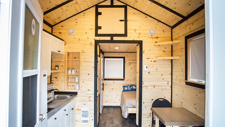 A photo of the interior of a tiny home, complete with a small kitchen and a bed in the background.