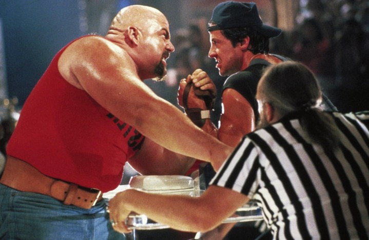 Two men arm wrestle in a competition with a ref looking on.