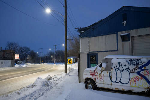 A picture of a white truck with graffiti on it, parked beside a building