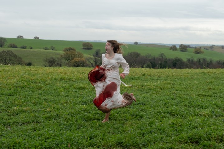 Sydney Sweeney runs through a field in a bloody dress in Immaculate.