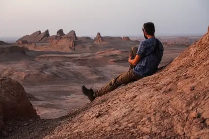 Junger Mann sitzt in der steinigen Lut Desert im Iran und schaut über die Wüste mit ihren spitzen Bergen