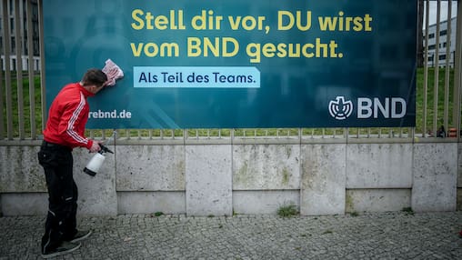 14.03.2024, Berlin: Ein Arbeiter säubert ein Plakat der neuen Imagekampagne des Bundesnachrichtendienstes (BND) mit der Aufschrift «Stell dir vor, du wirst vom BND gesucht» am Zaun der Zentrale des Dienstes. 

Normalerweise sucht der Bundesnachrichten-Dienst (BND) Kriminelle. Doch gerade sucht er auch neue Mitarbeiterinnen und Mitarbeiter. Darum geht auf diesem Plakat. (zu dpa: «Als Spion oder Spionin arbeiten») Foto: Kay Nietfeld/dpa - Honorarfrei nur für Bezieher des Dienstes dpa-Nachrichten für Kinder +++ dpa-Nachrichten für Kinder +++