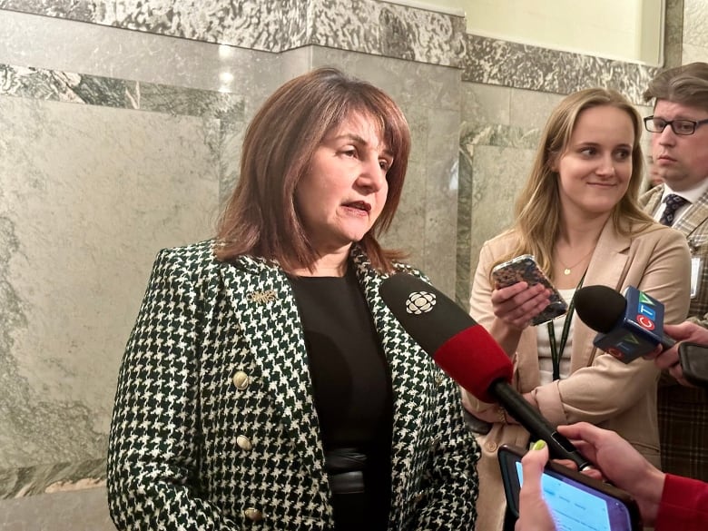 A woman in a black and white blazer speaks into a CBC News microphone.