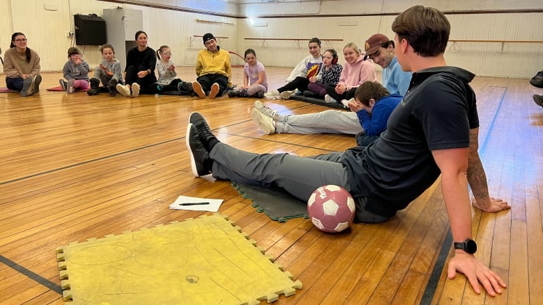 A group of children and university students are seated on a floor and gathered in a semi-circle.