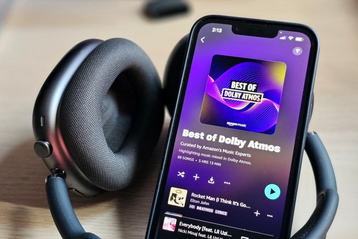 An iPhone 14 displaying the Amazon Music app with a Dolby Atmos Music playlist, next to a set of Apple AirPods Max headphones.