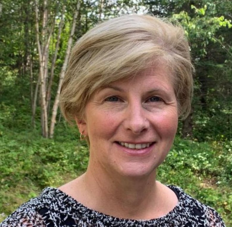 A smiling woman with blonde, chin length hair against a background of birch trees