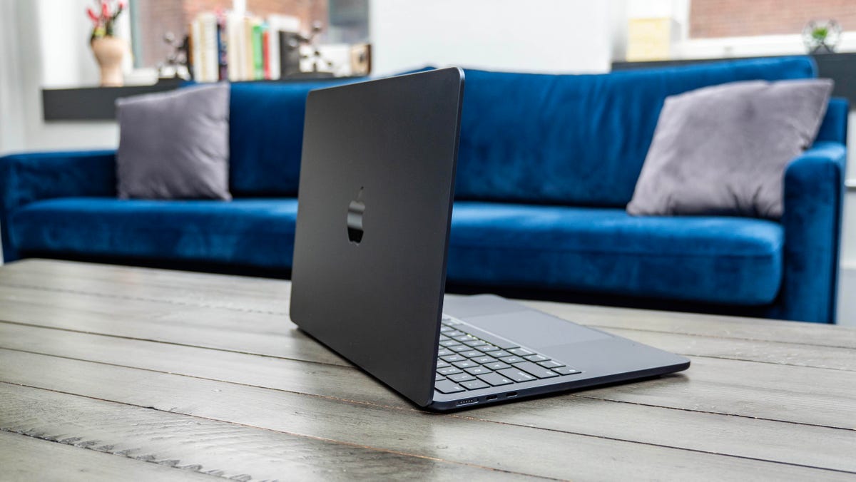 Apple MacBook Air M3 13-inch laptop on a wood table with a blue couch in the background.