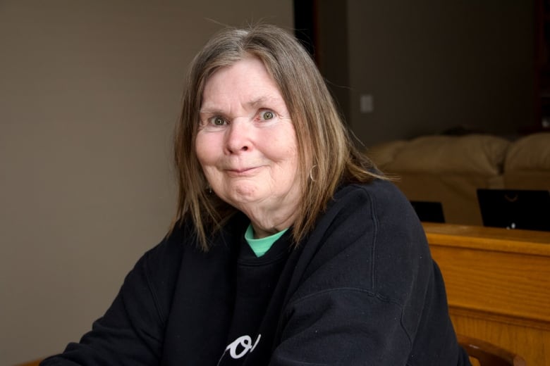 An older woman with shoulder-length, dark blonde hair and hazel eyes smiles at the camera.