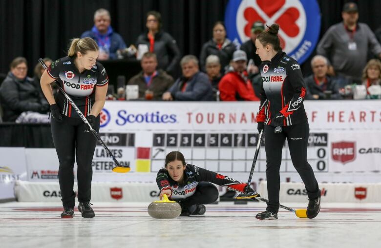 A curler sends a rock on the ice while two sweepers flank her.