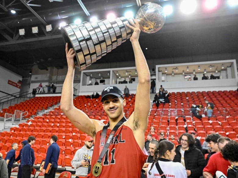 A men's basketball player raises a trophy.