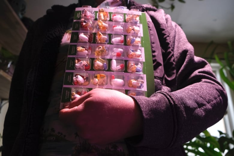 A hand is holding a medication holder with many different pills inside