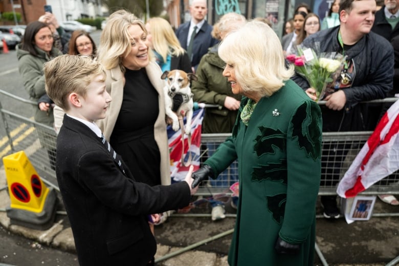 An adult shakes hands with a young person as another adult holding a dog looks on.